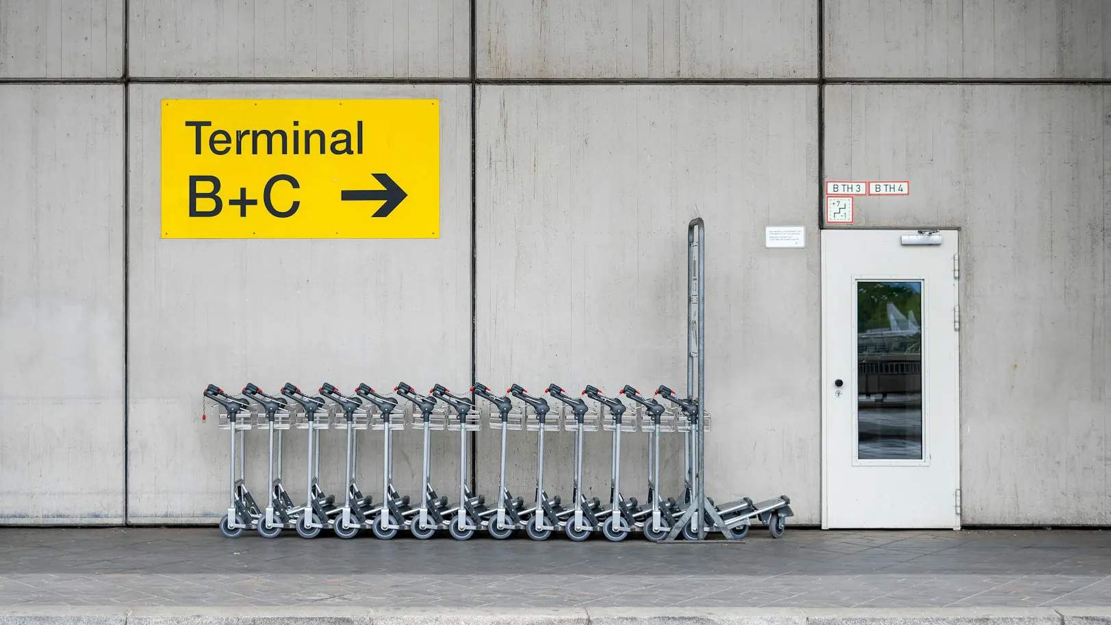 Ein paar Kofferwagen stehen vor einem Wegweiser am Flughafen.